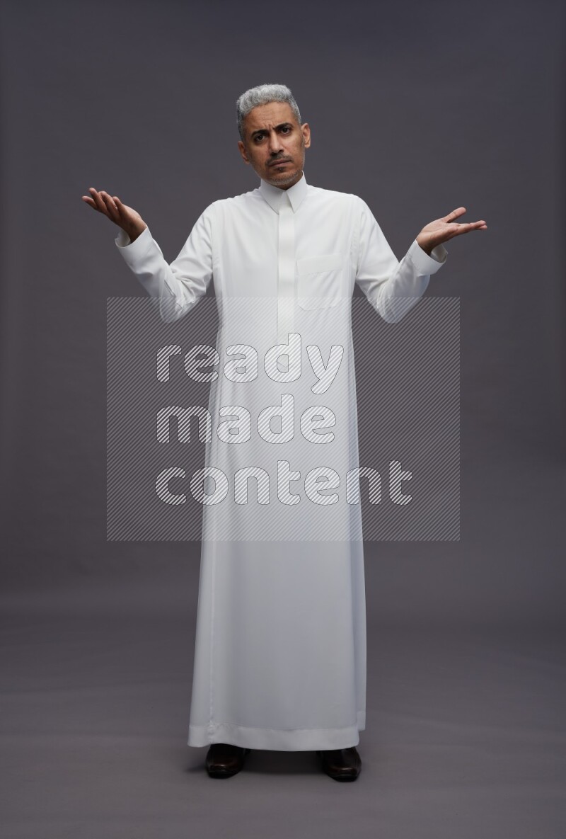 Saudi man wearing thob standing interacting with the camera on gray background
