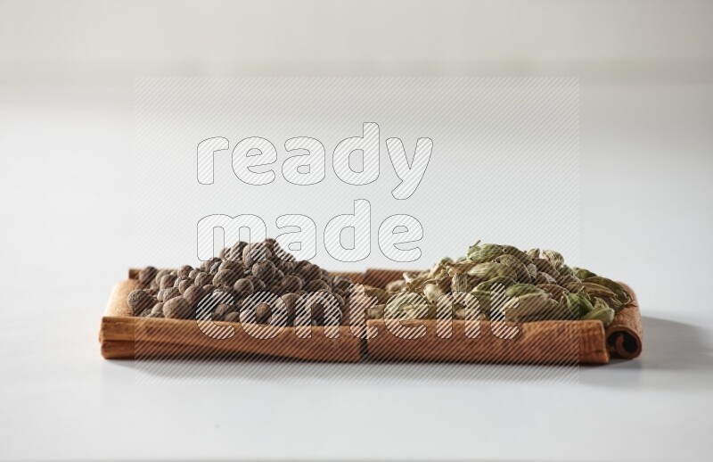 مربعان من أعواد القرفة ممتلئان بحبوب الهيل وحبوب الفلفل الحلو علي خلفية بيضاء