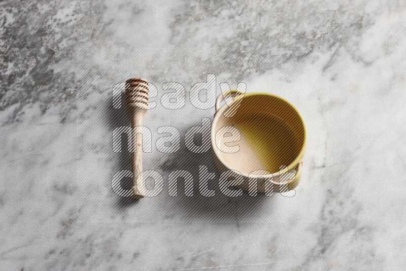 Multicolored pottery bowl with wooden honey dipper on the side on grey marble background