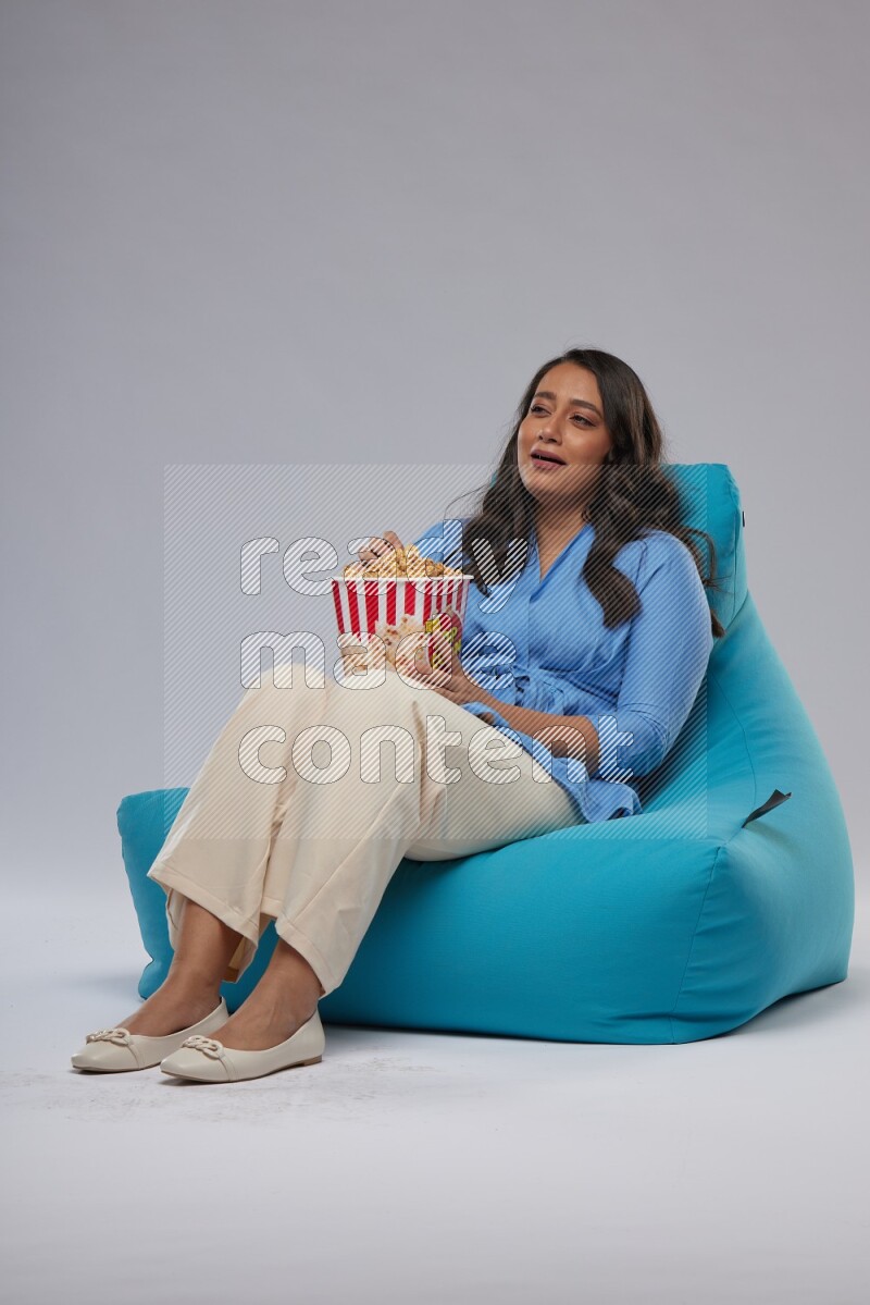 A woman sitting on a blue beanbag and eating popcorn