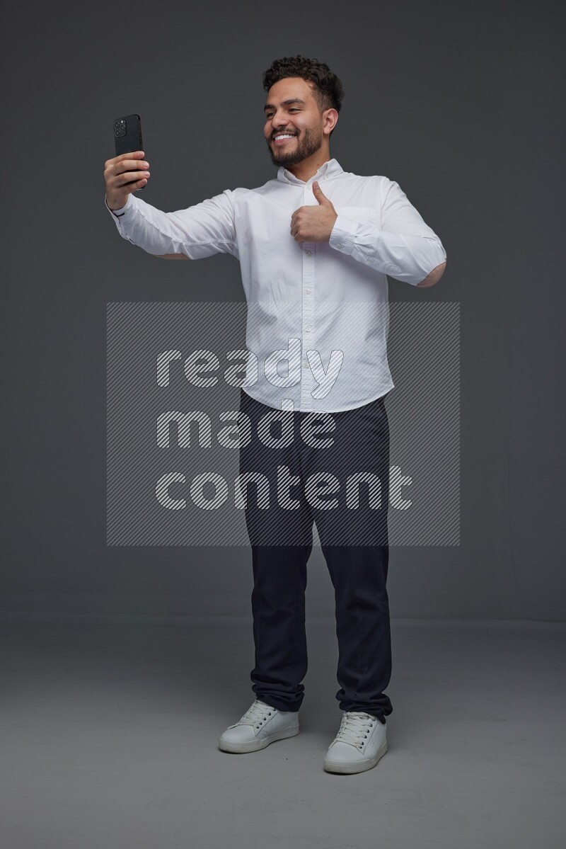 A man wearing smart casual and taking selfie with his phone eye level on a gray background