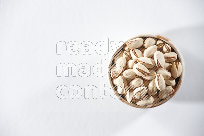 A beige ceramic bowl full of pistachios on a white background in different angles