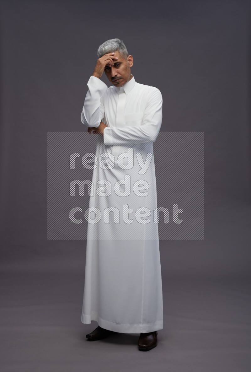Saudi man wearing thob standing interacting with the camera on gray background