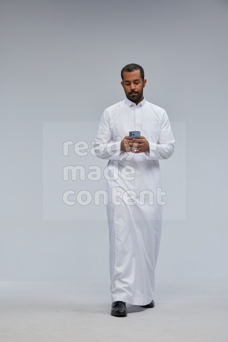 Saudi man wearing Thob standing texting on phone on Gray background