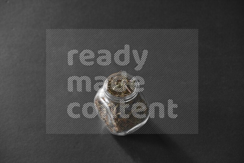 A glass spice jar full of basil on black flooring