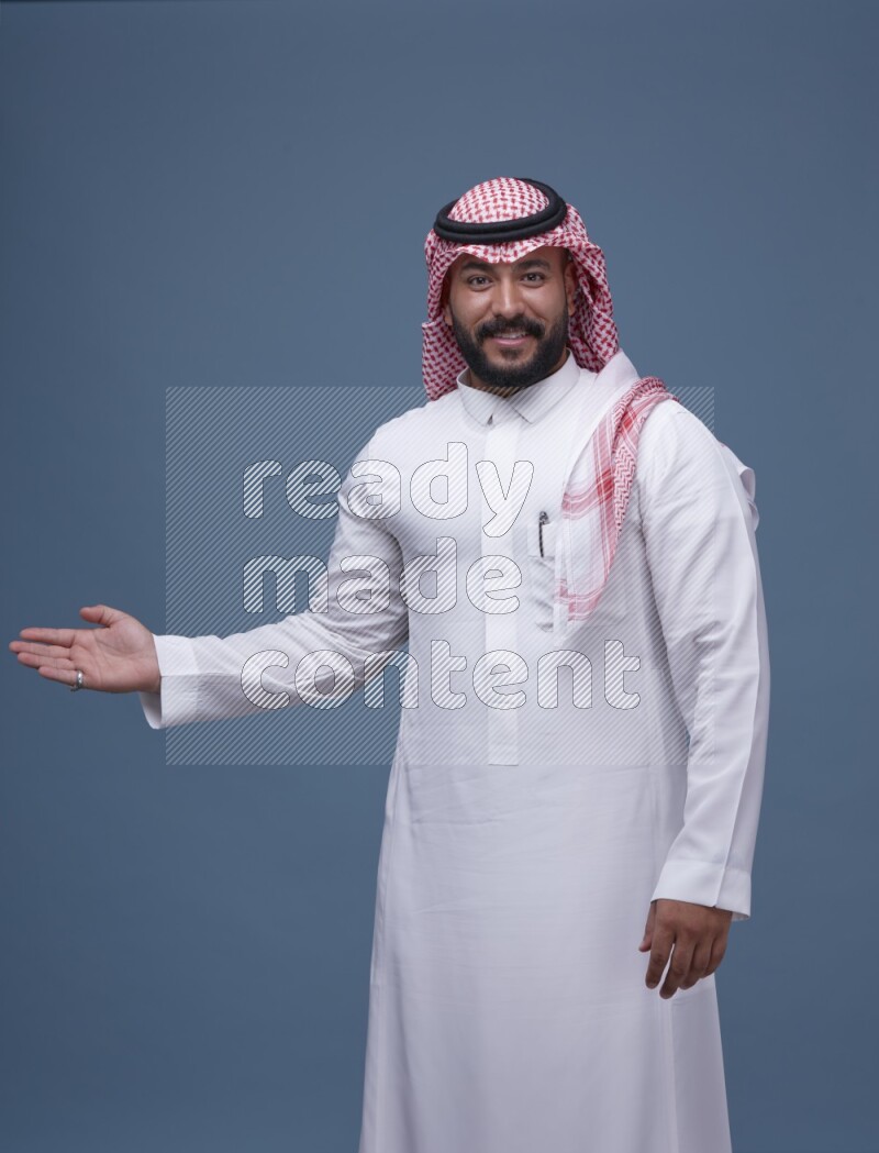 A man pointing on blue background wearing Saudi Thob with Shomag