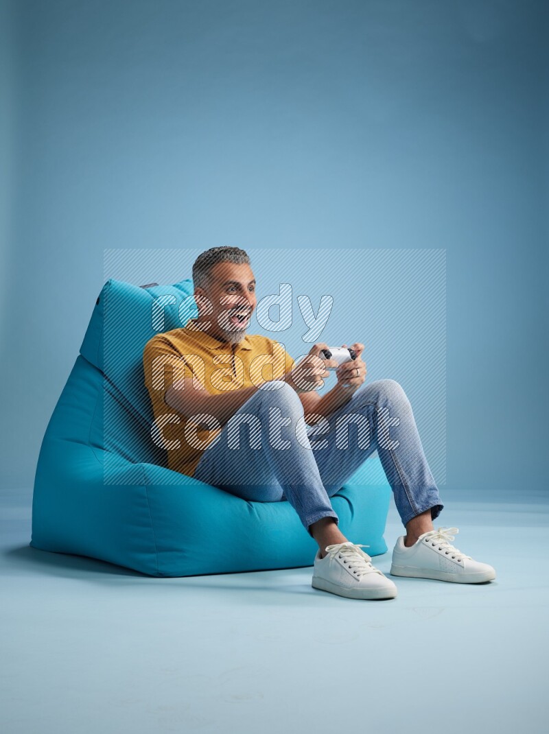 A man sitting on a blue beanbag and gaming with joystick