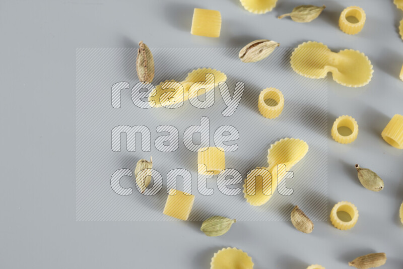 Raw pasta with different ingredients such as cherry tomatoes, garlic, onions, red chilis, black pepper, white pepper, bay laurel leaves, rosemary, cardamom and mushrooms on light blue background