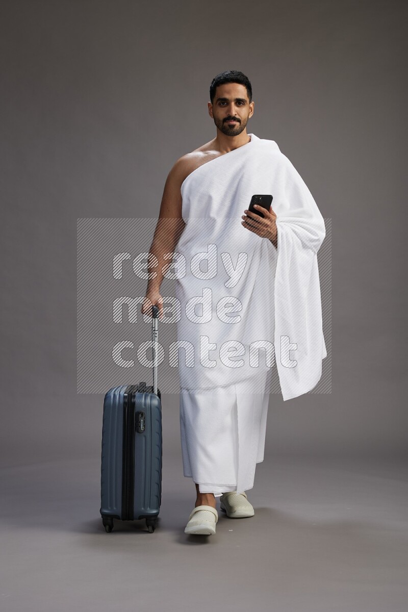 A man wearing Ehram Standing holding traveling bag on gray background