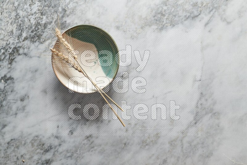 Wheat stalks on multicolored pottery plate on grey marble background