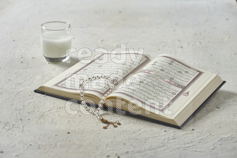 Quran with dates, prayer beads and different drinks all placed on textured white background