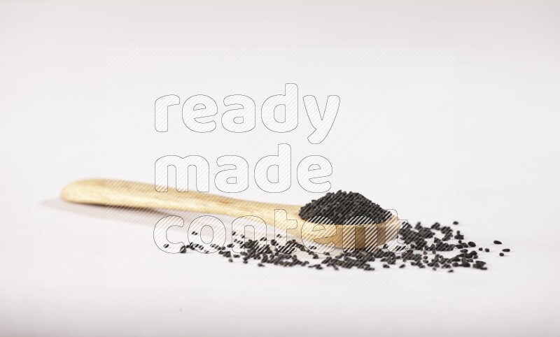 A wooden spoon full of black seeds on a white flooring