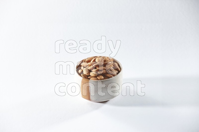 A beige ceramic bowl full of peeled almonds on a white background in different angles