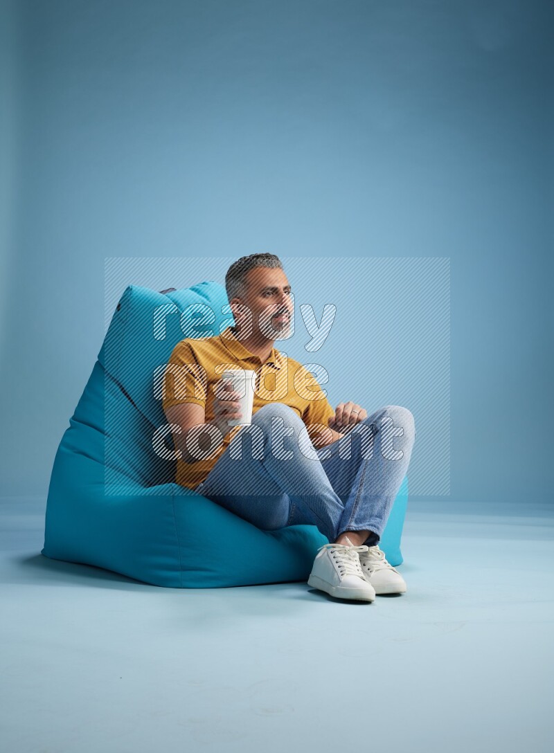 A man sitting on a blue beanbag and drinking coffee