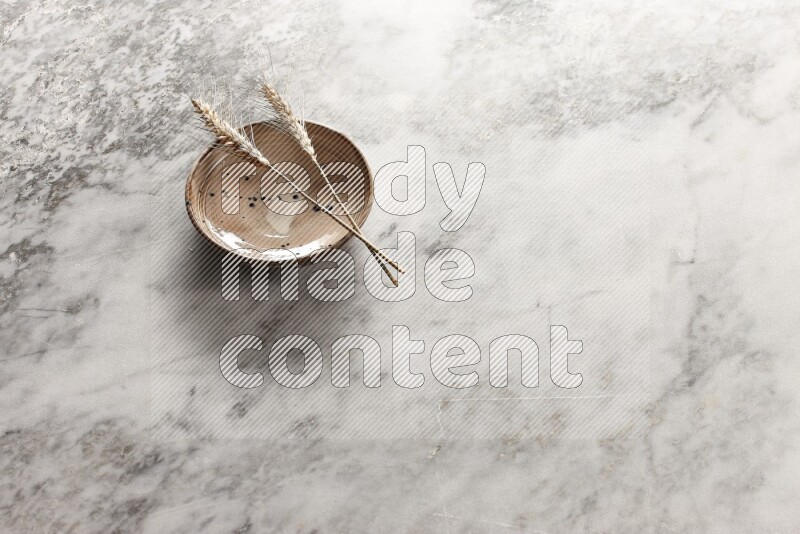 Wheat stalks on multicolored pottery bowl on grey marble background