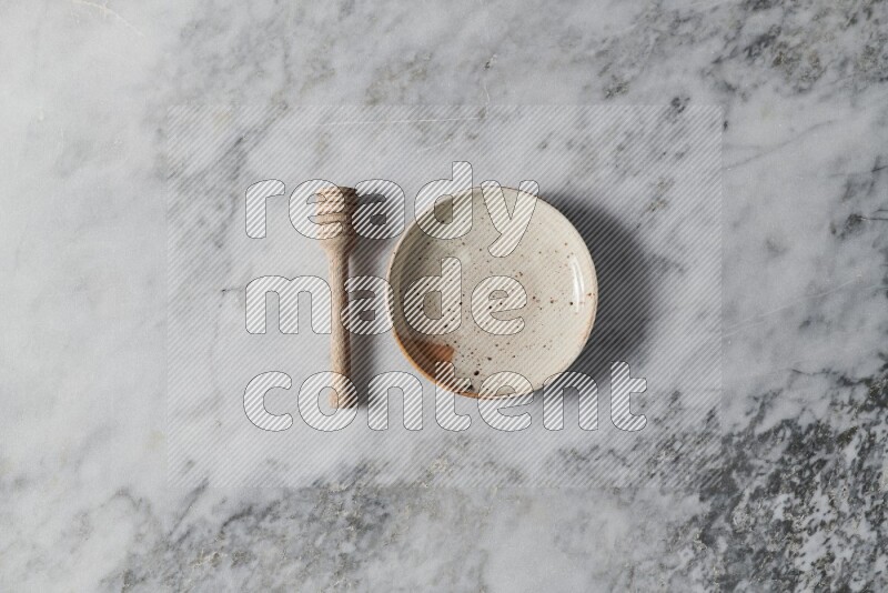 Multicolored pottery plate with wooden honey dipper on the side on grey marble background