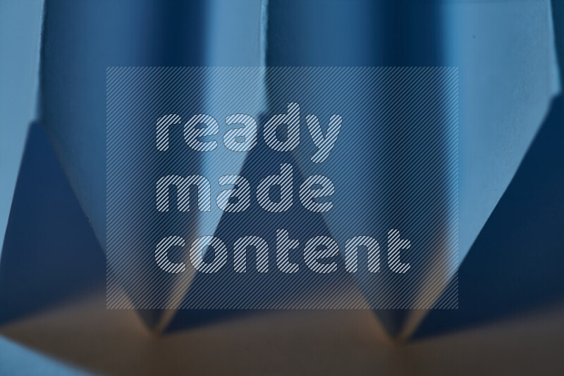 A close-up abstract image showing sharp geometric paper folds in blue gradients and warm tones