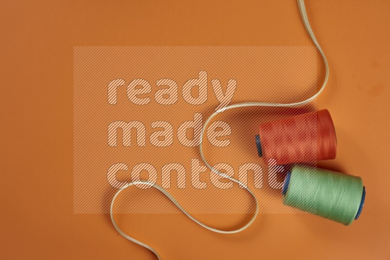 مجموعة من أدوات الخياطة والتفصيل خضراء وبرتقالية اللون على خلفية برتقالية