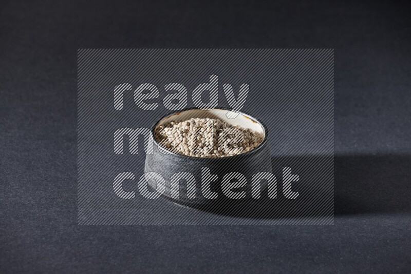 Black pottery bowl full of white pepper on black flooring