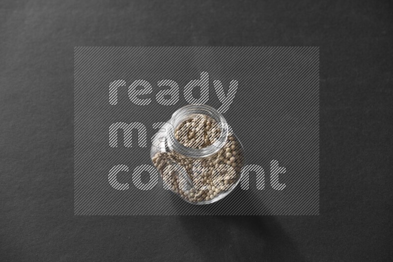 A glass spice jar full of white peppers on black flooring