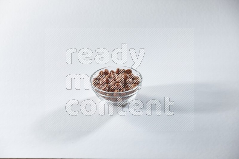 A glass bowl full of peeled hazelnuts on a white background in different angles