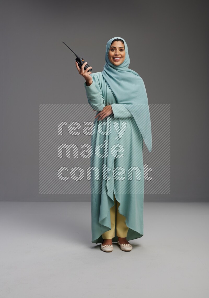 Saudi Woman wearing Abaya standing holding walkie-talkie on Gray background