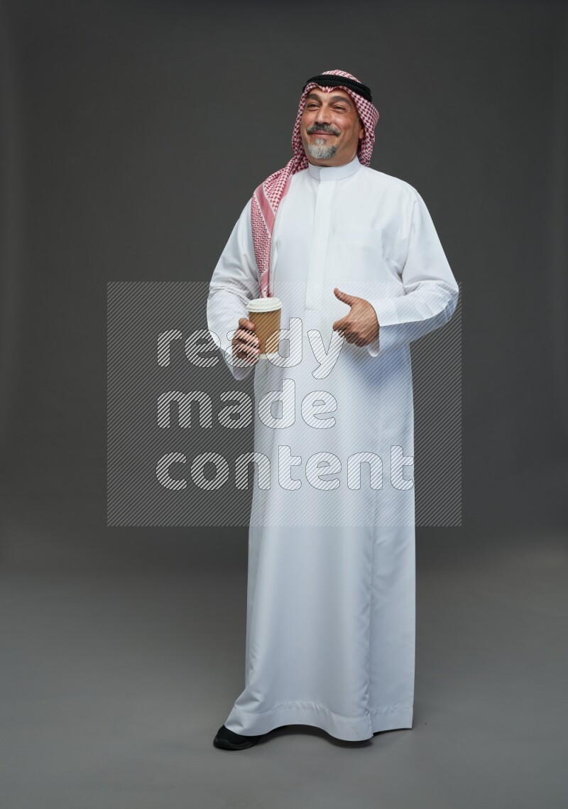 Saudi man with shomag Standing holding paper cup on gray background