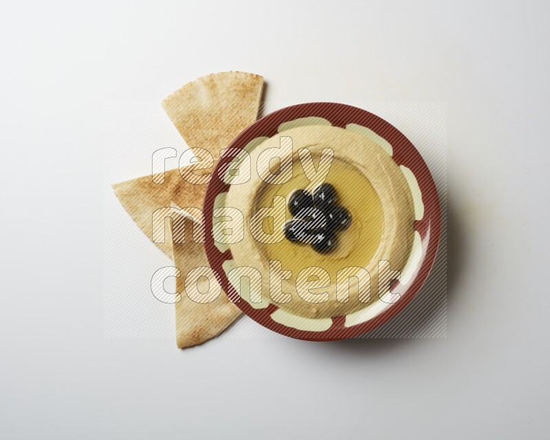 Hummus in a traditional plate garnished with black olives on a white background