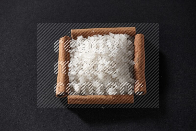 أربعة من أعواد القرفة مكونة شكل مربع بداخلها ملح أبيض علي خلفية سوداء