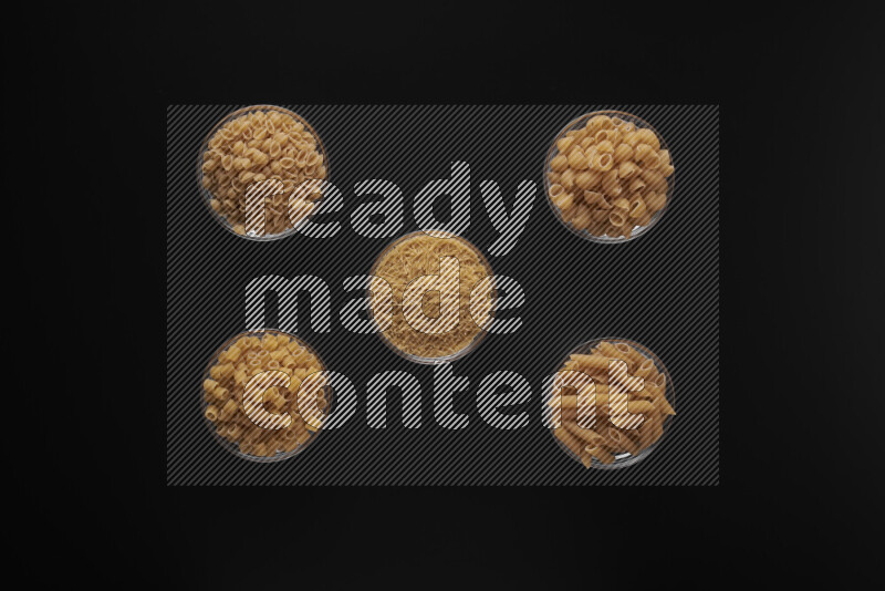 Different pasta types in 5 glass bowls on black background