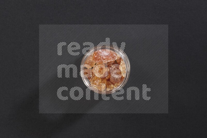 A glass jar full of gum arabic on black flooring