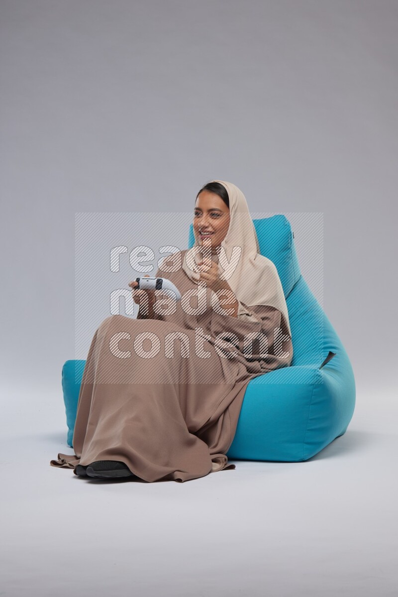 A Saudi woman sitting on a blue beanbag and gaming with joystick