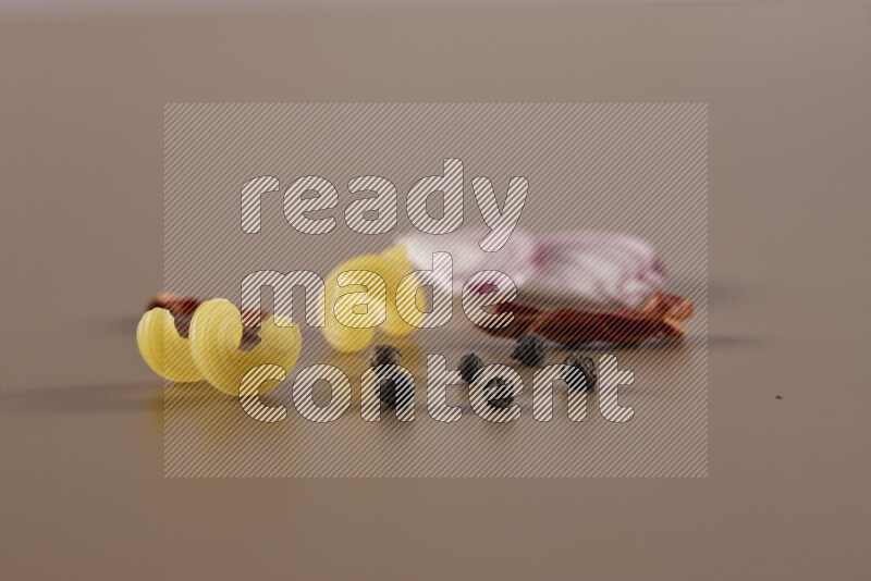 Raw pasta with different ingredients such as cherry tomatoes, garlic, onions, red chilis, black pepper, white pepper, bay laurel leaves, rosemary and cardamom on beige background