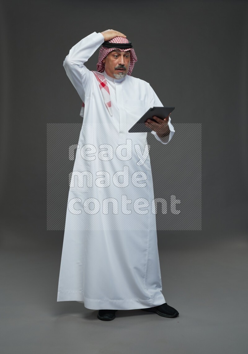 Saudi man with shomag Standing working on tablet on gray background