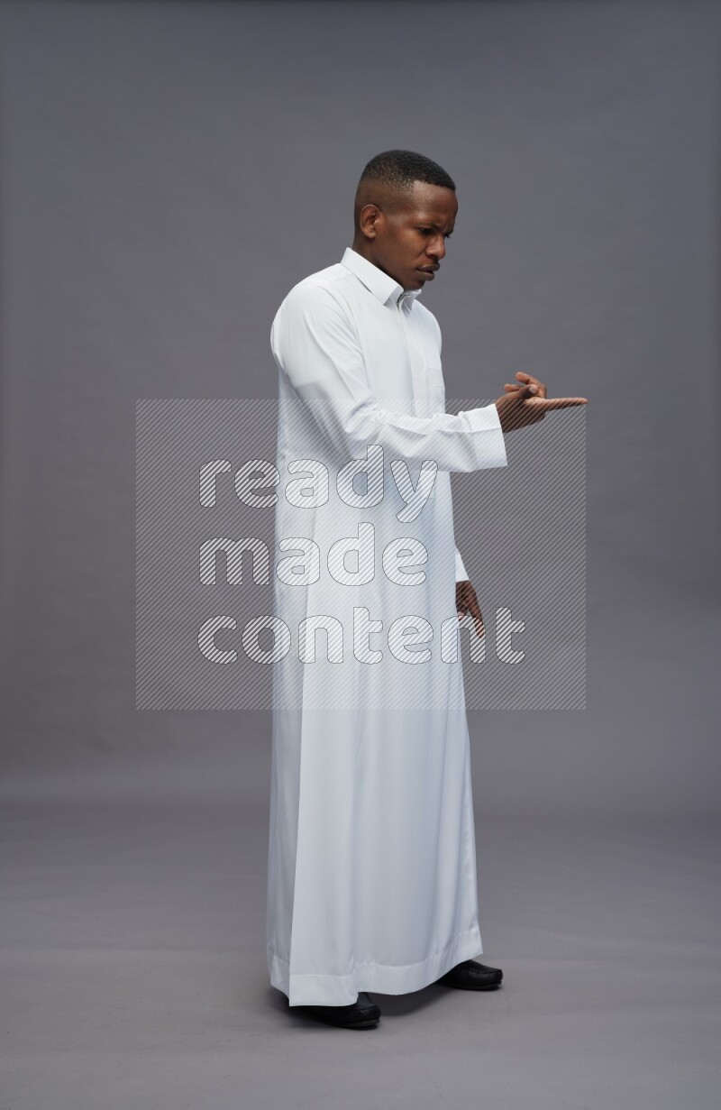 Saudi man wearing thob standing interacting with the camera on gray background
