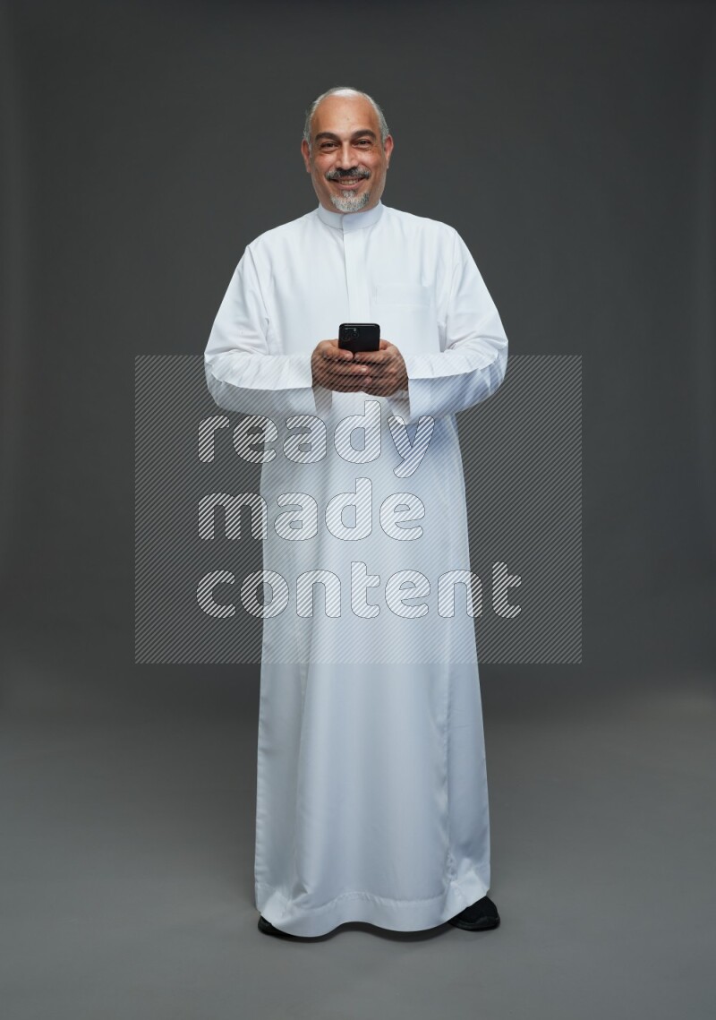Saudi man without shomag Standing texting on phone on gray background
