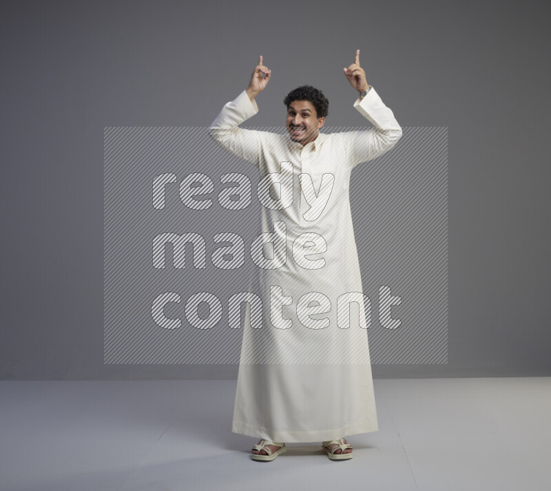 A Saudi man standing wearing thob interacting with the camera on gray background