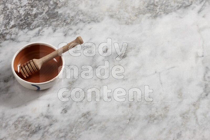 Multicolored pottery bowl with wooden honey dipper in it on grey marble background