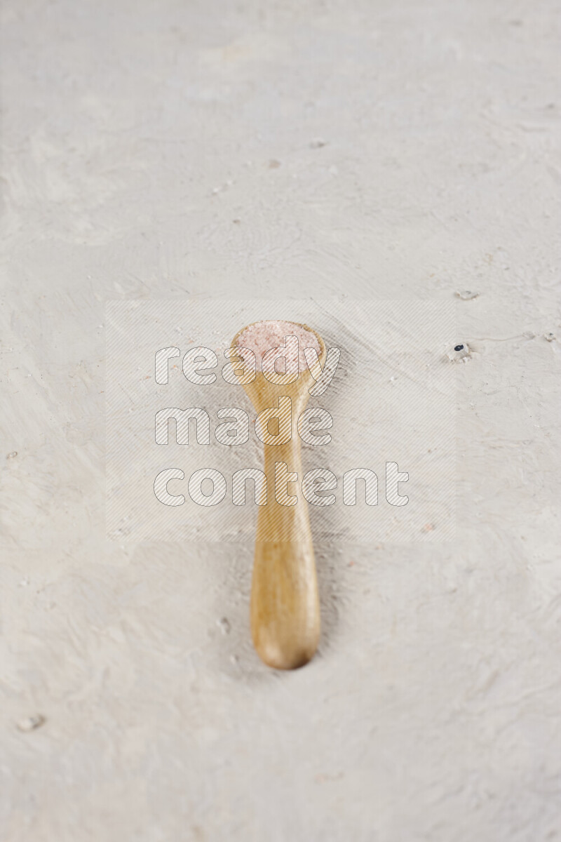 A wooden spoon full of pink himalayan salt on white background