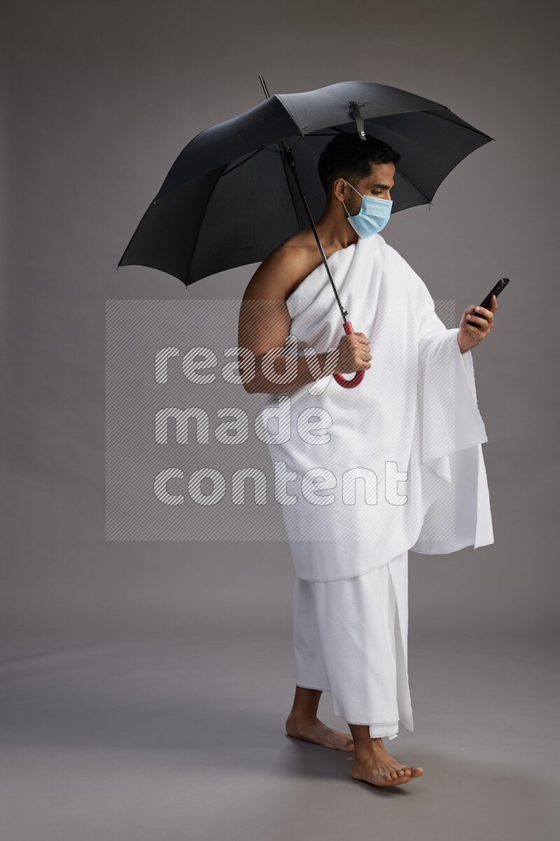 A man wearing Ehram and mask Standing holding umbrella on gray background on gray background