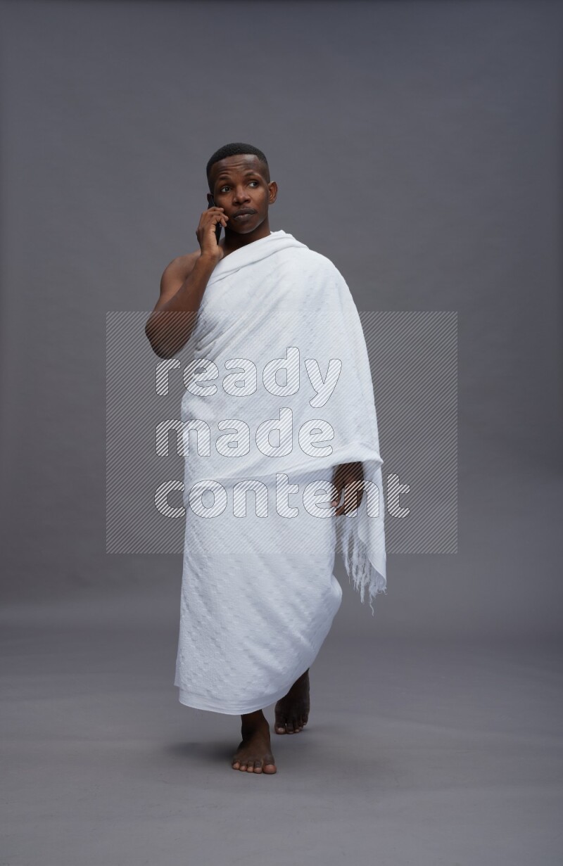 A man wearing Ehram Standing talking on phone on gray background