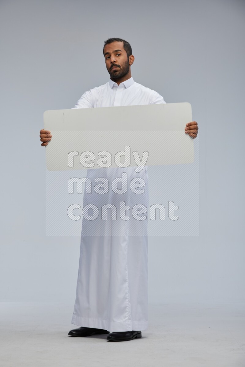 Saudi man wearing Thob standing holding board on Gray background