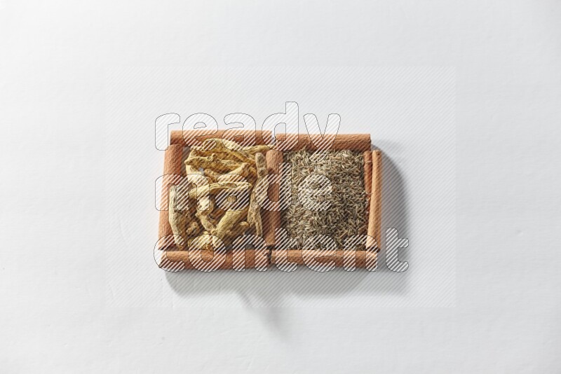 مربعان من أعواد القرفة ممتلئان بحبوب الكمون وأصابع الكركم علي خلفية بيضاء