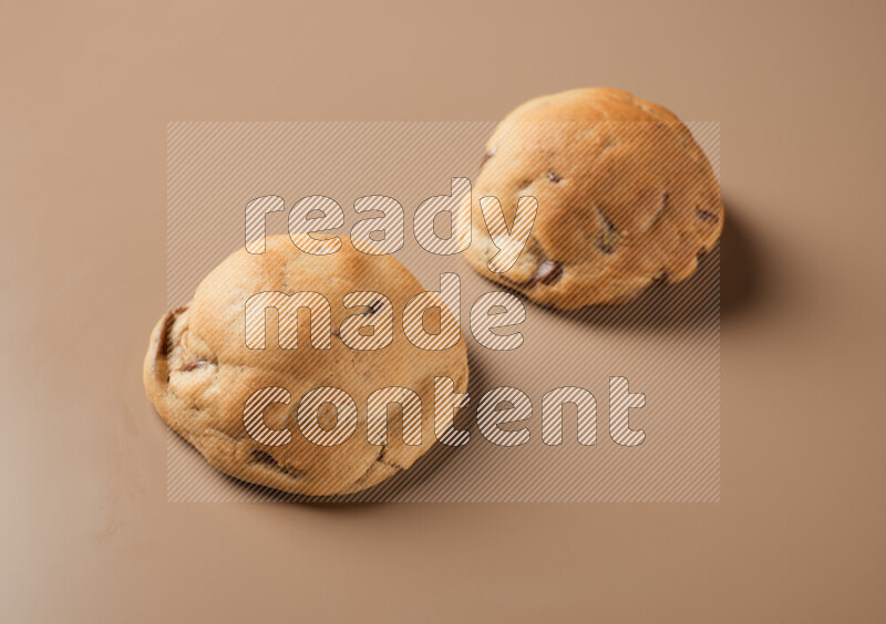 Two chocolate chip cookies on a brown background