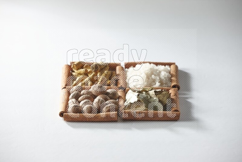 4 مربعات من أعواد القرفة ممتلئة بالملح وورق الغار وجوزة الطيب والكركم على أرضية بيضاء