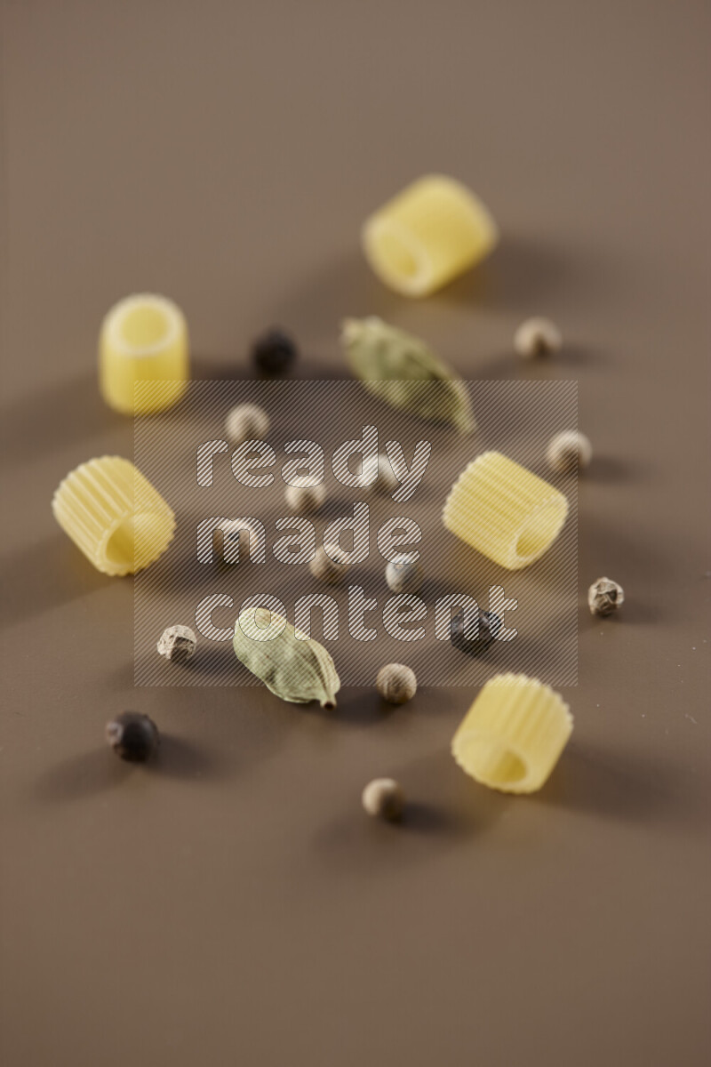 Raw pasta with different ingredients such as cherry tomatoes, garlic, onions, red chilis, black pepper, white pepper, bay laurel leaves, rosemary and cardamom on beige background