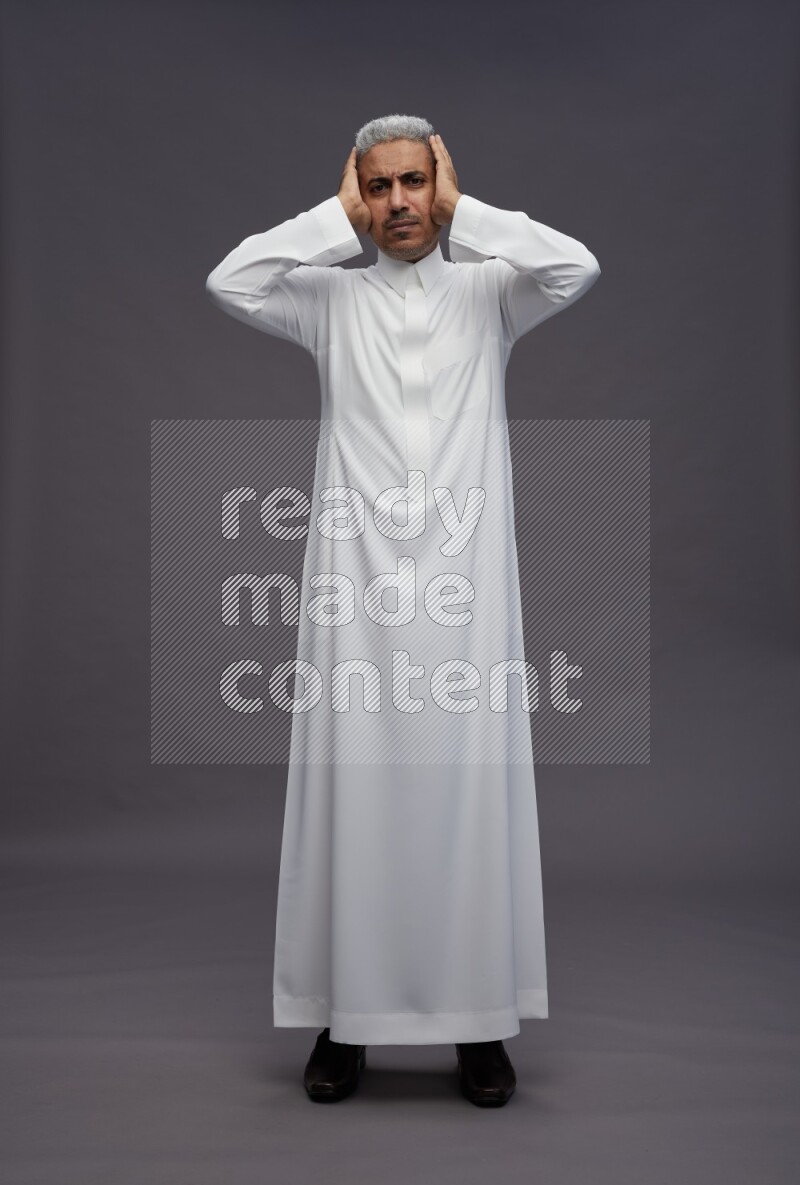 Saudi man wearing thob standing hands behind head on gray background