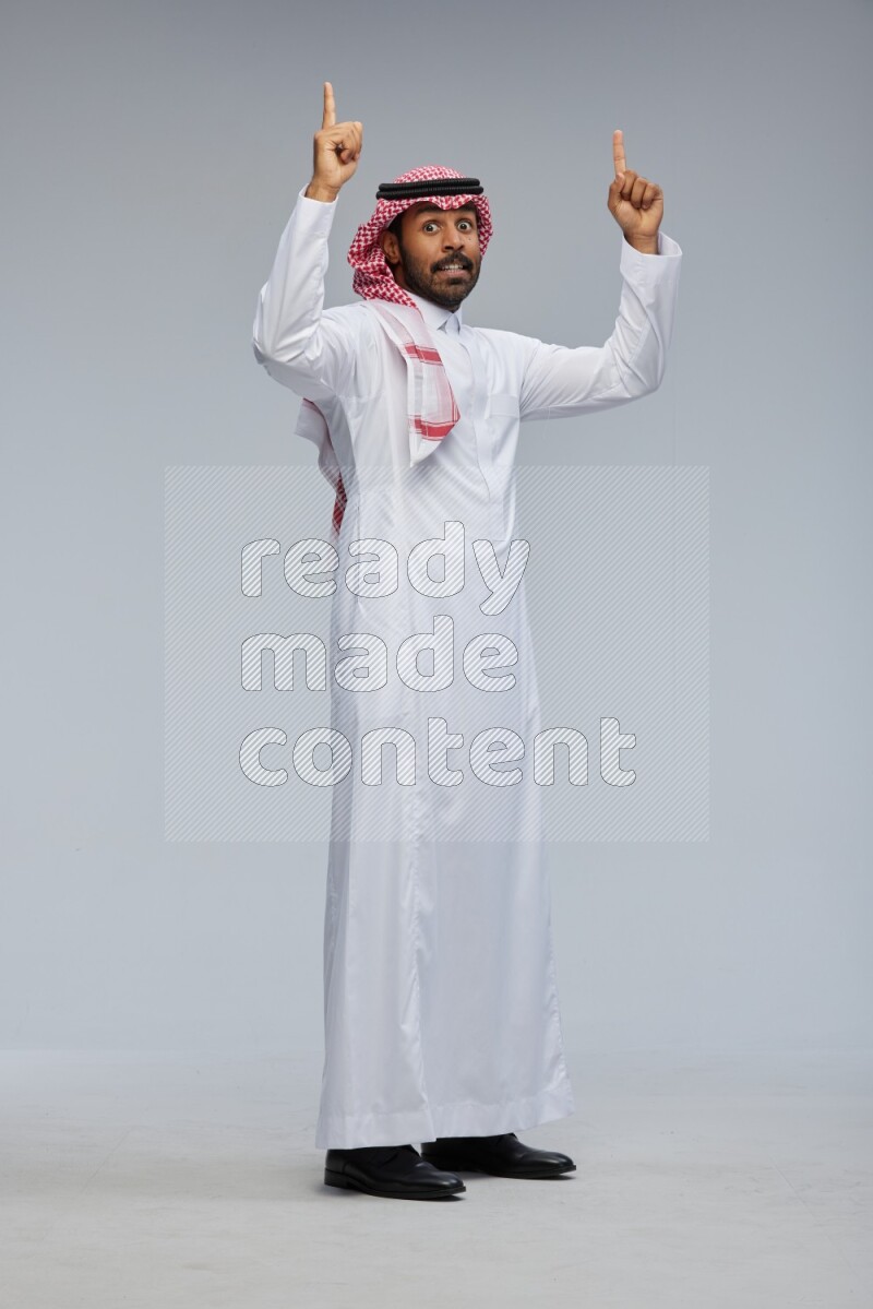 Saudi man Wearing Thob and shomag standing interacting with the camera on Gray background