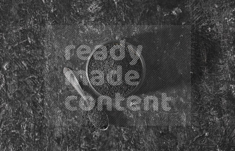 وعاء فخاري أسود وملعقة معدنية ممتلئان ببذور حبة البركة علي خلفية سوداء