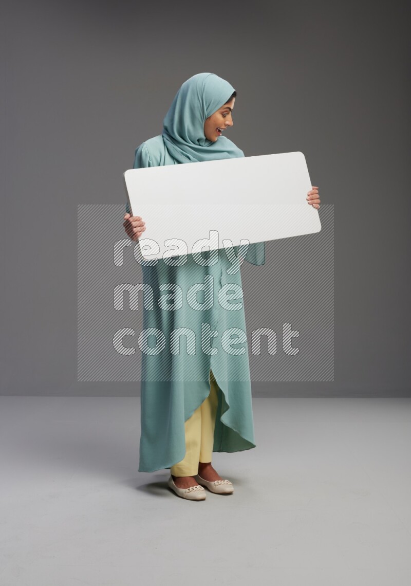 Saudi Woman wearing Abaya standing holding board on Gray background